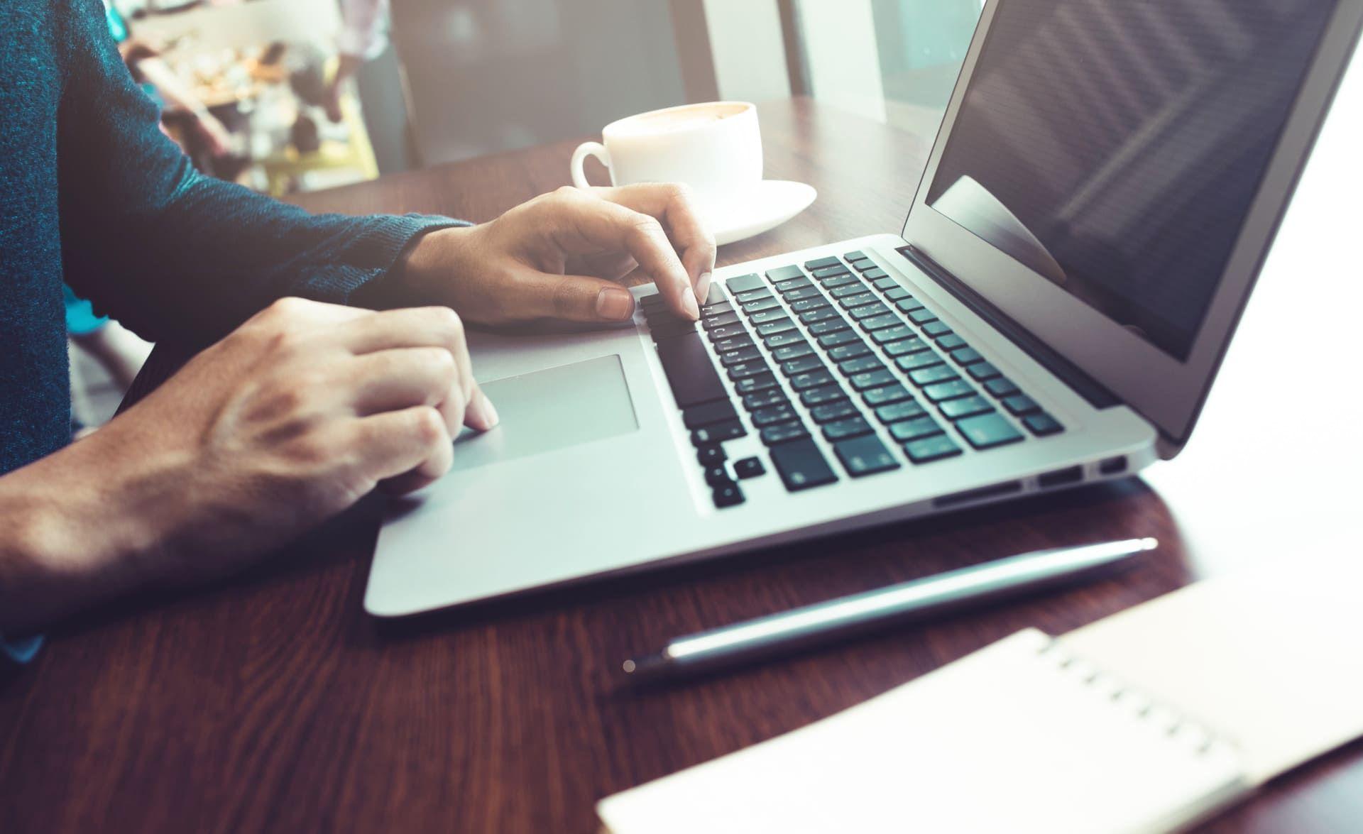 Persona utilizando una notebook que está sobre un escritorio junto a una taza de café